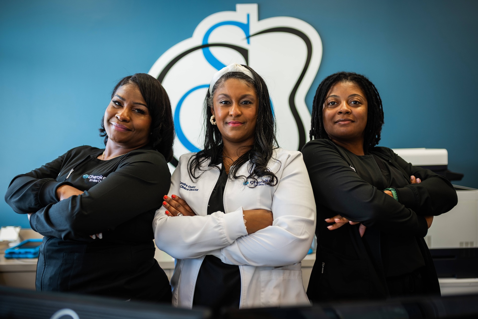 Three women standing together with their arms crossed, posing for a photo in an office setting.