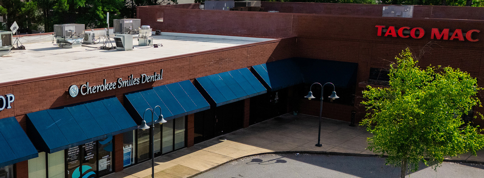 The image shows a storefront with a Taco Mac restaurant sign, featuring a large building with a prominent brick facade and multiple awnings, including one with a blue canopy.