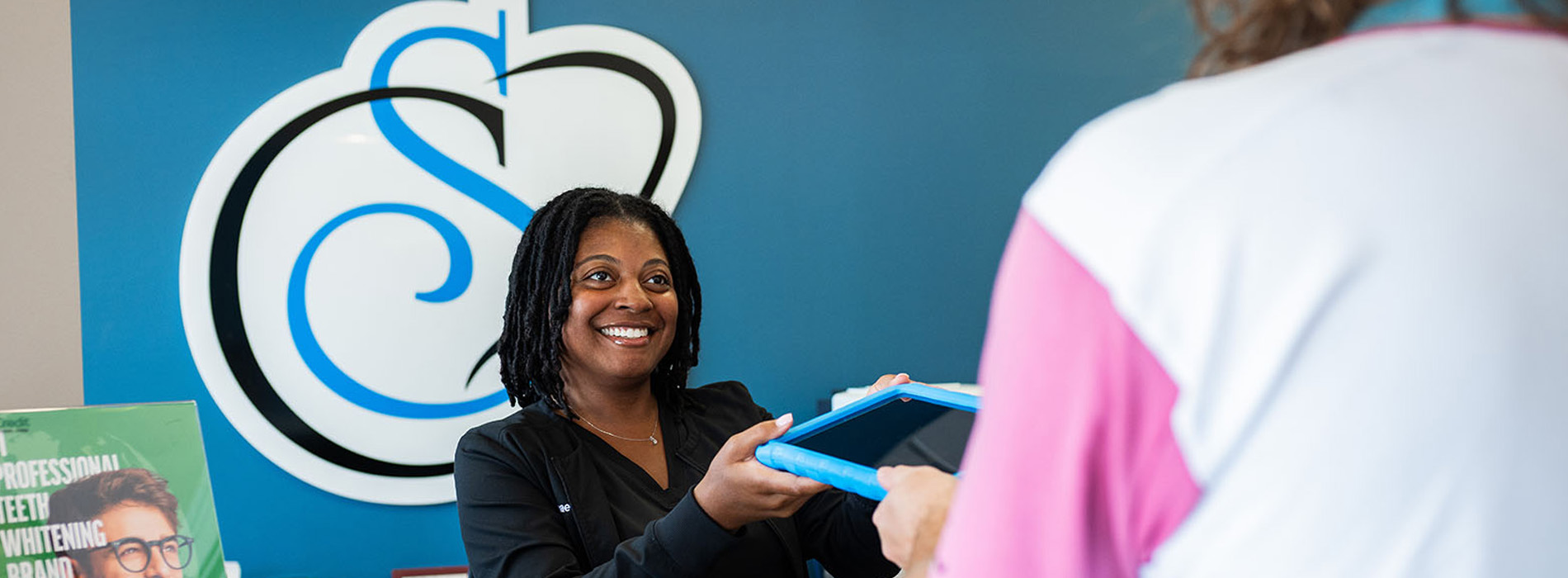 A person holding blue tubes in front of a sign with white text, possibly at an event or gathering.