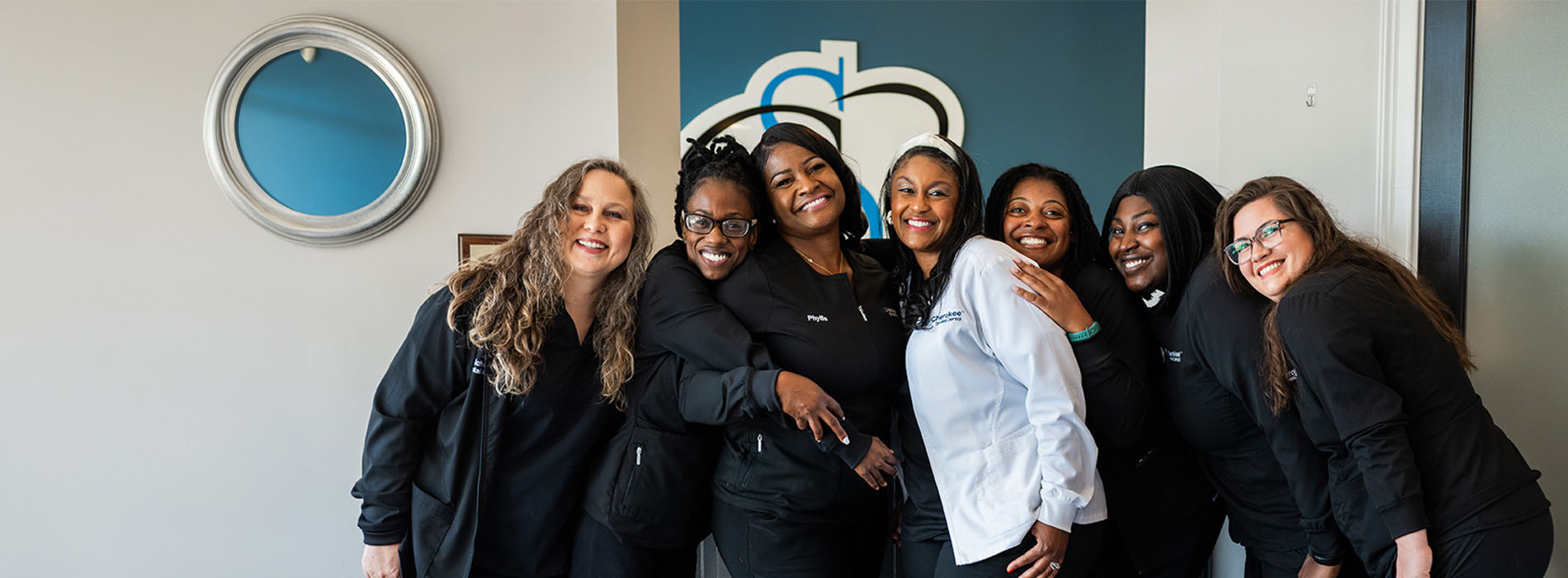 The image shows a group of people posing together with smiles, likely for a team photo, in front of a sign with a logo.