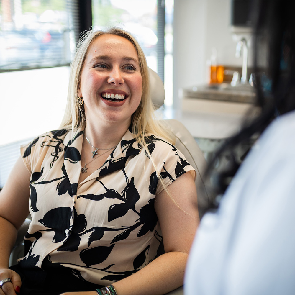 A woman with blonde hair and a black and white top smiling at a dental office receptionist.
