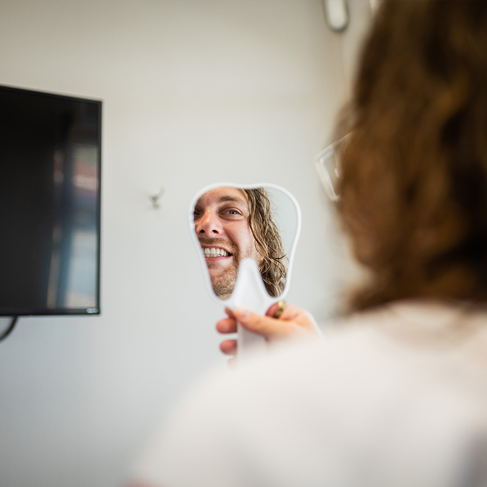 A person holding up a mirror with their reflection smiling at the camera.