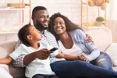 A family of four sharing a moment together on a couch, with two adults and two children, smiling and looking at something off-camera.