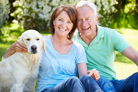 An elderly couple sitting outdoors with a dog, smiling at the camera.