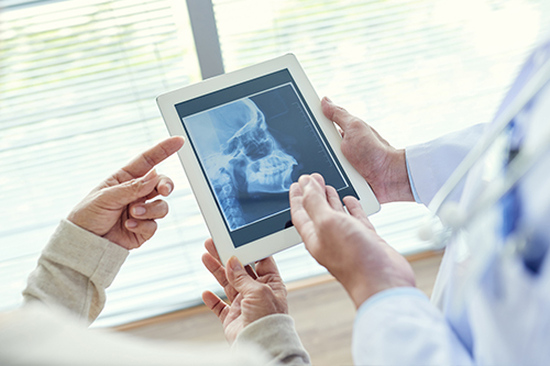 This is a photograph showing two individuals looking at a tablet displaying an X-ray image while standing in a medical setting, with one person seemingly pointing at something on the screen.