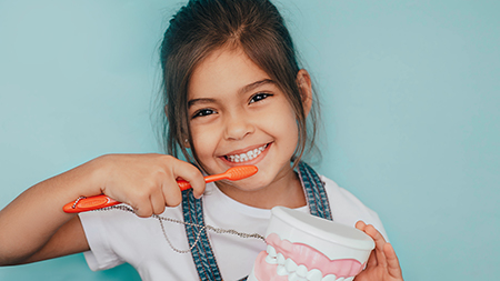 Girl brushing her teeth with an electric toothbrush, smiling while holding the brush in her mouth.