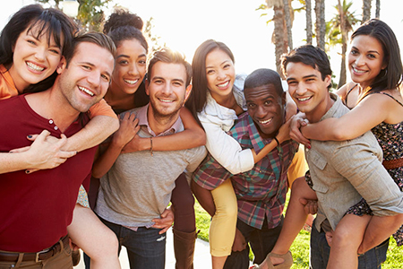 A group of young adults posing for a photo with smiles on their faces, standing outdoors during daylight hours.